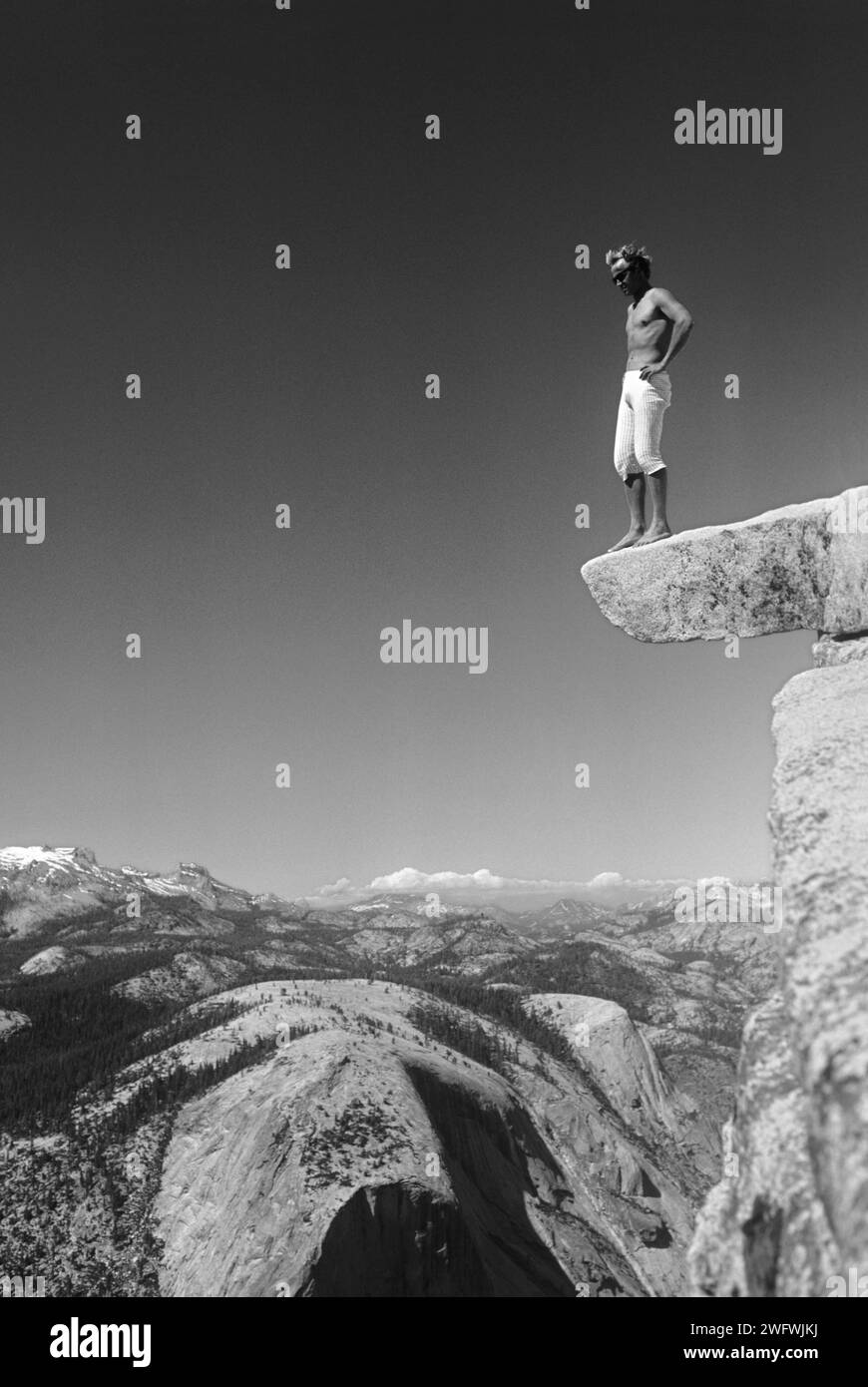 Der junge Mann riskiert sein Leben und steht auf einem Felsvorsprung auf dem Gipfel des Half Dome im Yosemite Valley, Kalifornien, USA Stockfoto