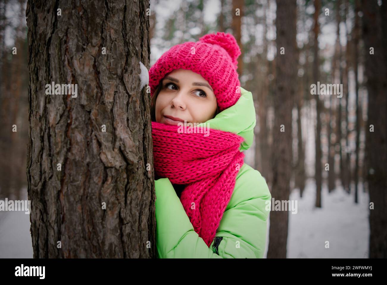 Frau in grüner Jacke und rosafarbenem Schal, die sich an einen Baum lehnt. Stockfoto
