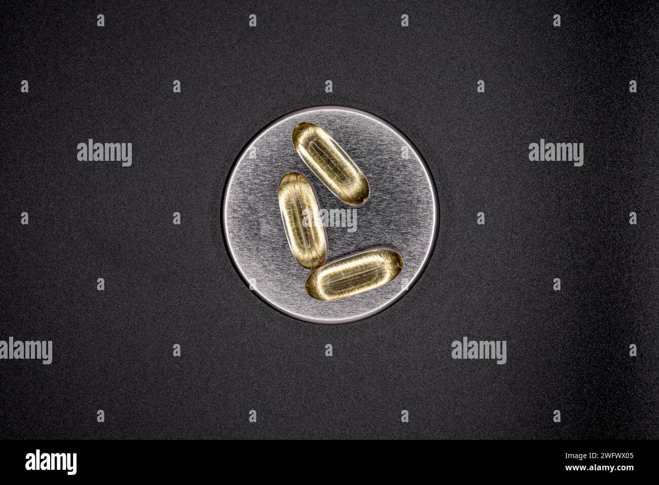 Omega 3 Fischöl-Gelkapseln auf einer Aluminiumkappe auf einem neutralen schwarzen Hintergrund. CSB-Lebertabletten. Drei von kontrastreichem Omega 3-6-9. Stockfoto