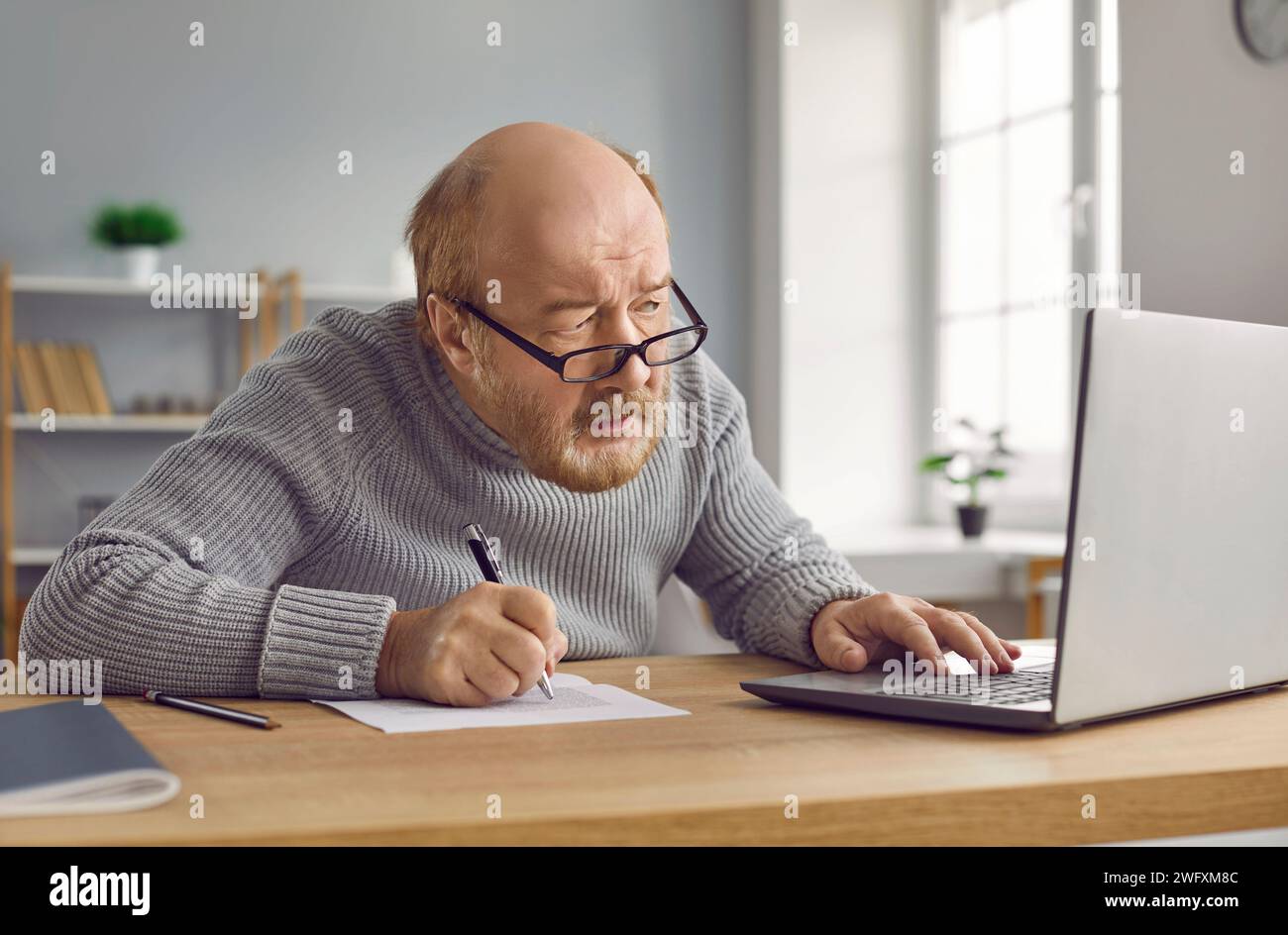 Ein älterer Mann mit Brille, der auf den Laptop-Bildschirm schaut Stockfoto
