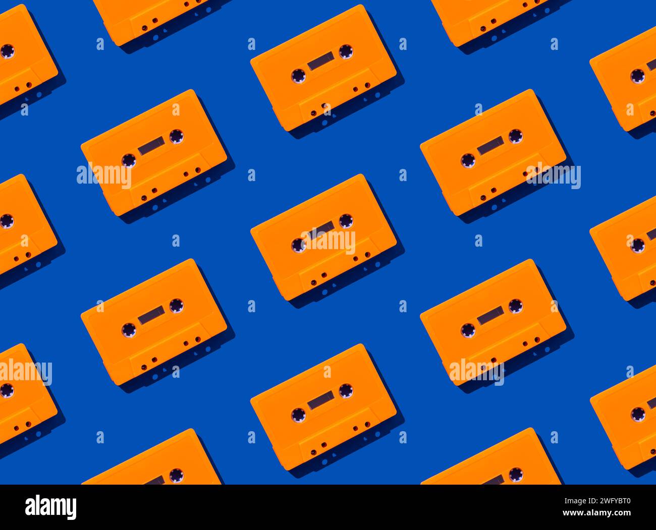 Muster mit orangen Retro-Audiokassetten auf blauem Hintergrund. Kreatives Konzept der Retro-Technologie. Ästhetik der 80er Jahre. Vintage-Audio Stockfoto