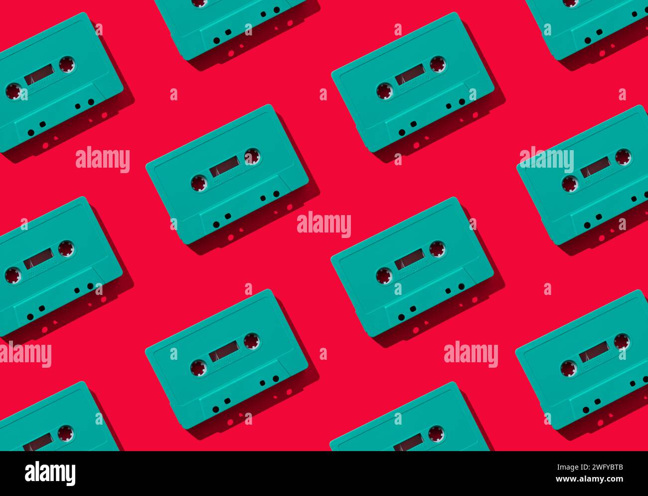 Muster mit grünen Retro-Audiokassetten auf rotem Hintergrund. Kreatives Konzept der Retro-Technologie. Ästhetik der 80er Jahre. Vintage-Audio Stockfoto