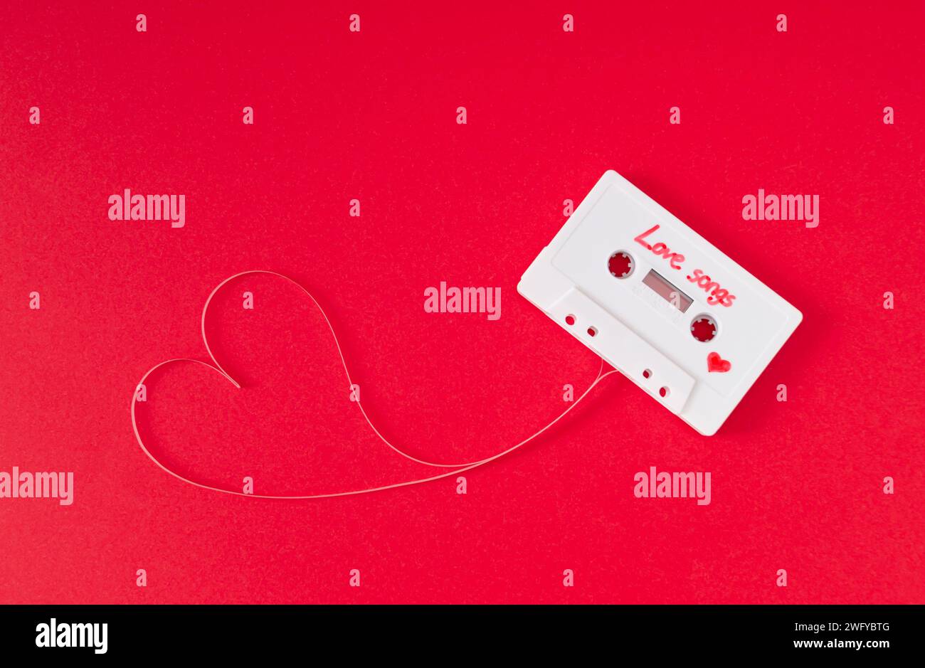 Audiokassette mit losem Band, das ein Herz auf rotem Hintergrund bildet. Minimales Liebeskonzept. Liebeskarte mit kreativer Retro-Technologie. Ästhetik der 80er Jahre. Stockfoto