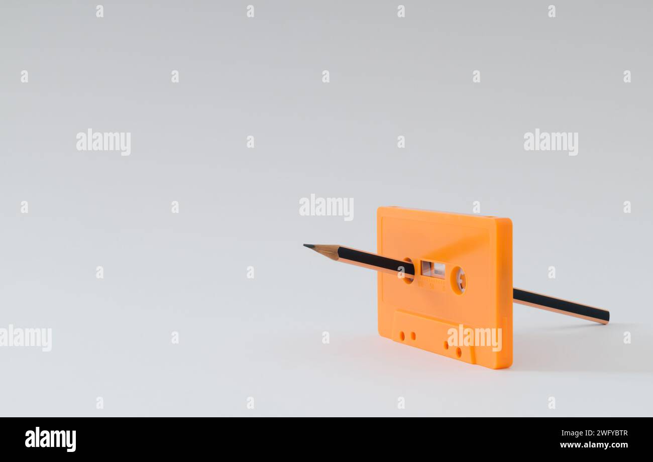 Du bist der Bleistift für mein Kassettenband. Altes orangefarbenes Audiokassettenband und Bleistift auf weißem Hintergrund. Manueller Rücklauf. Minimales Kassettenbandkonzept. Stockfoto