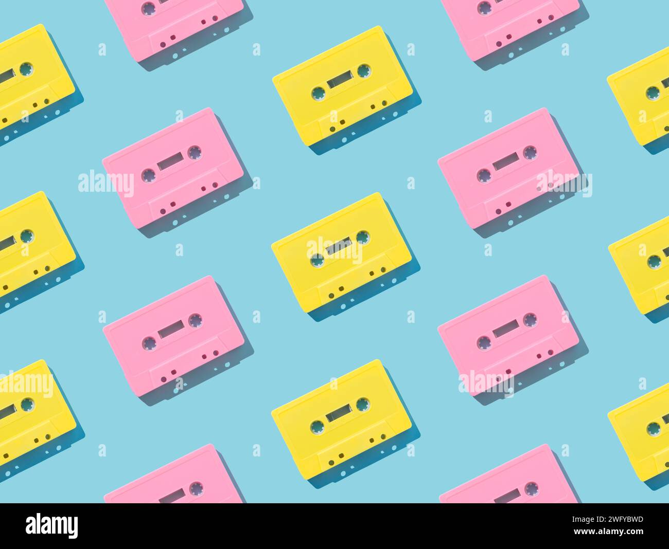 Muster von rosafarbenen und gelben Tonkassettenbändern im Retro-Look auf blauem Hintergrund. Kreatives Konzept der Retro-Technologie. Ästhetik der 80er Jahre. Vintage-Audio Stockfoto