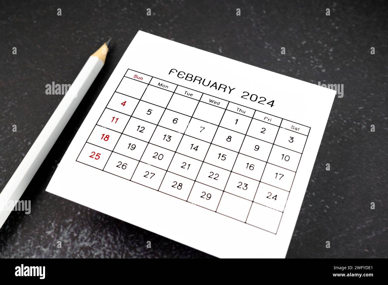 Weiße Kalenderseite für Februar 2024 und Bleistift auf schwarzem Hintergrund. Stockfoto