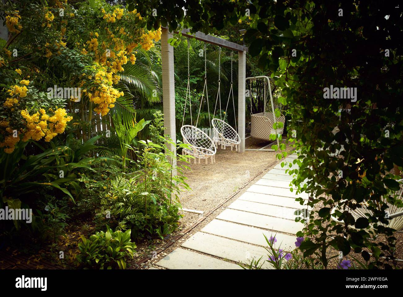 Weißer Boho-Schaukelstuhl im Freien mit niemandem in einem wunderschönen, entspannenden und gemütlichen Garten Stockfoto