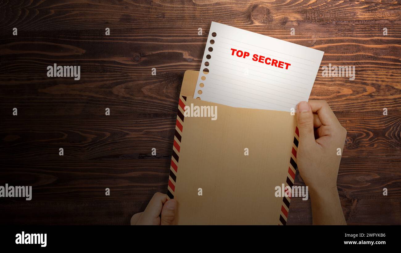 Eine menschliche Hand öffnet einen braunen Umschlag mit dem Text "Top-Secret" auf dem Papier. Geheimes Konzept Stockfoto