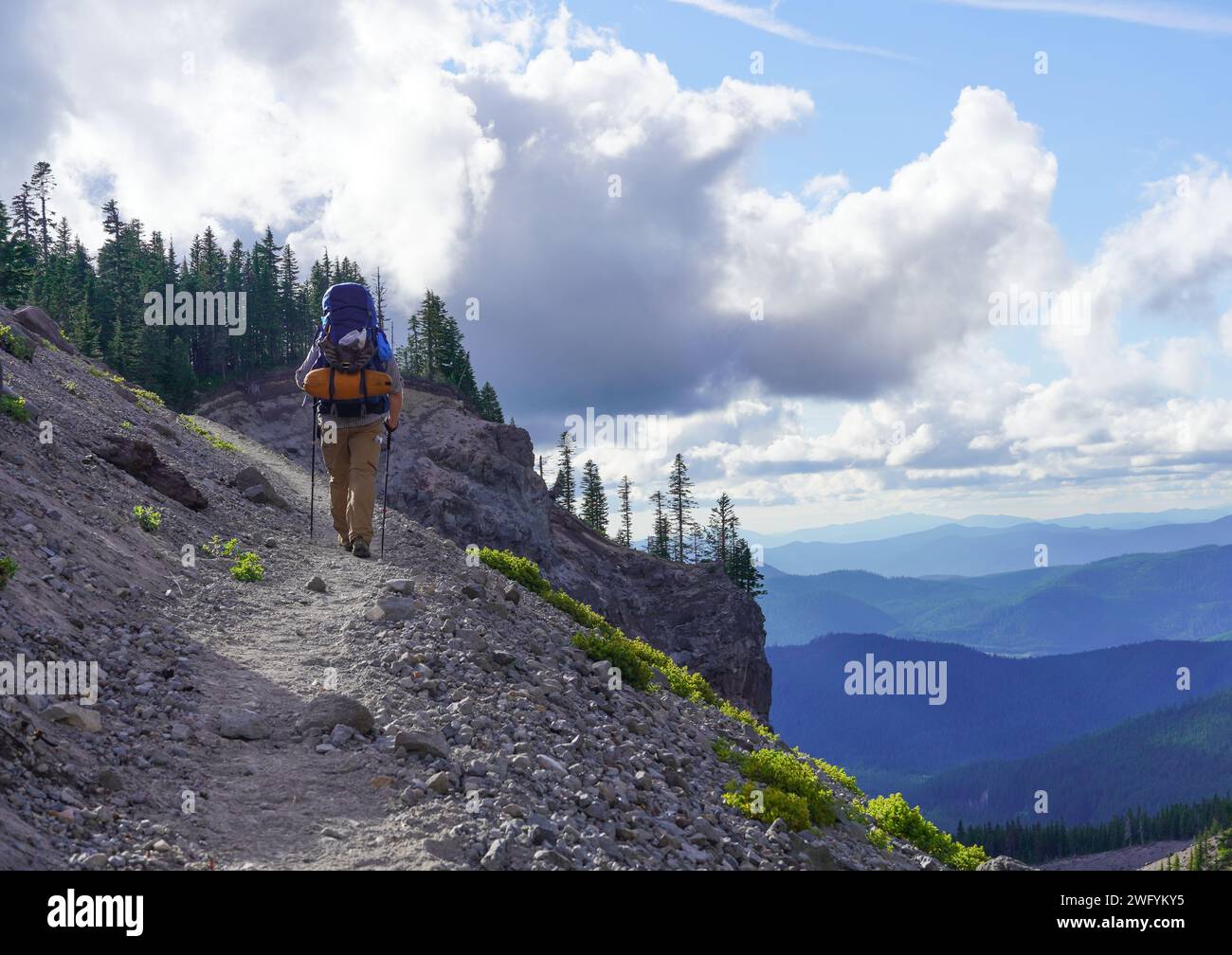 Ein Mann in seinen 50ern, der am späten Nachmittag eine felsige Steigung hinaufwandert. Eine Schlafkissen und Campingausrüstung sind am Rucksack festgeschnallt zu sehen. Stockfoto