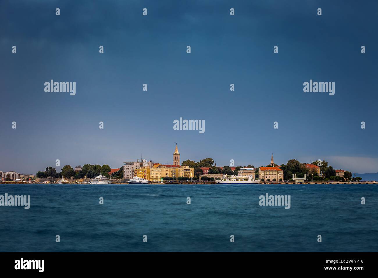 Zadar, Kroatien - Panoramablick auf die Altstadt von Zadar bei Sonnenuntergang mit beleuchteter Kathedrale von St. Anastasia Glockenturm, Yachten und Fähre Stockfoto