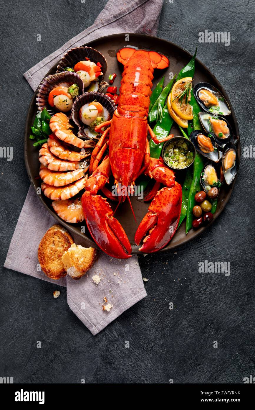 Großer roter Hummer auf Teller mit Garnelen und Muscheln mit Zitrone, Souce Pesto und Brot. Meeresfrüchte-Konzept. Draufsicht. Stockfoto