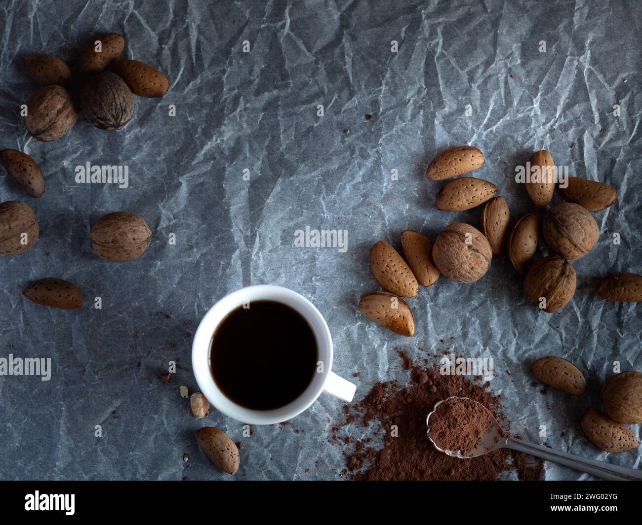 Eine Tasse Kaffee und eine Auswahl an Nüssen auf einem Tisch mit Wachspapier. Stockfoto