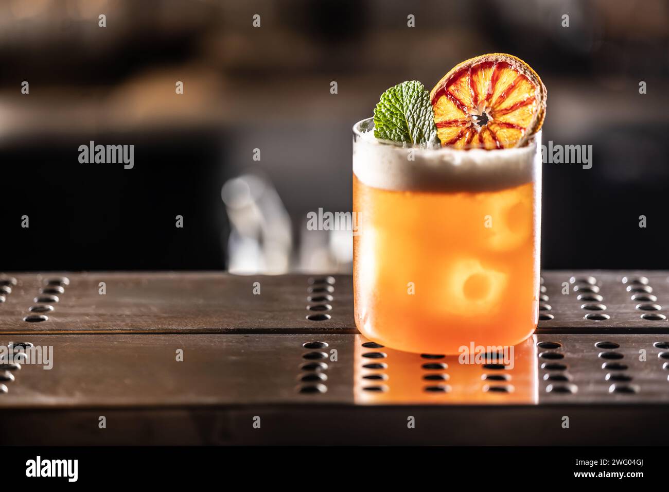 Ein Glas Jungle Bird Cocktail garniert mit getrockneten roten Orangen- und Minzblättern an der Bar. Stockfoto