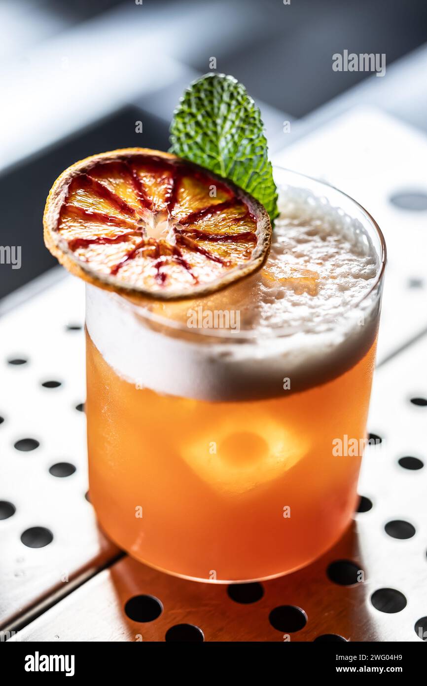 Ein Glas Jungle Bird Cocktail garniert mit getrockneten roten Orangen- und Minzblättern an der Bar. Stockfoto