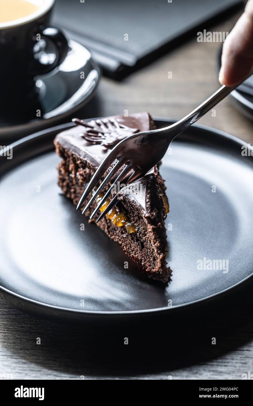 Ein Gast in einem Café schneidet einen Sacherkuchen mit einer Gabel. Stockfoto