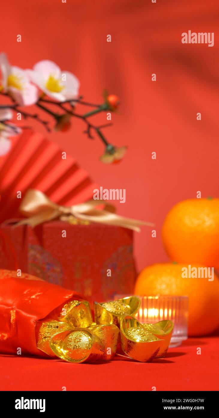 Chinesischer roter Hintergrund für das Mondneujahr. Alte chinesische Barren in Seidentüte, rote Geschenkbox mit goldener Schleife, Papierfächer, Orangen, Pflaumenblüte Stockfoto