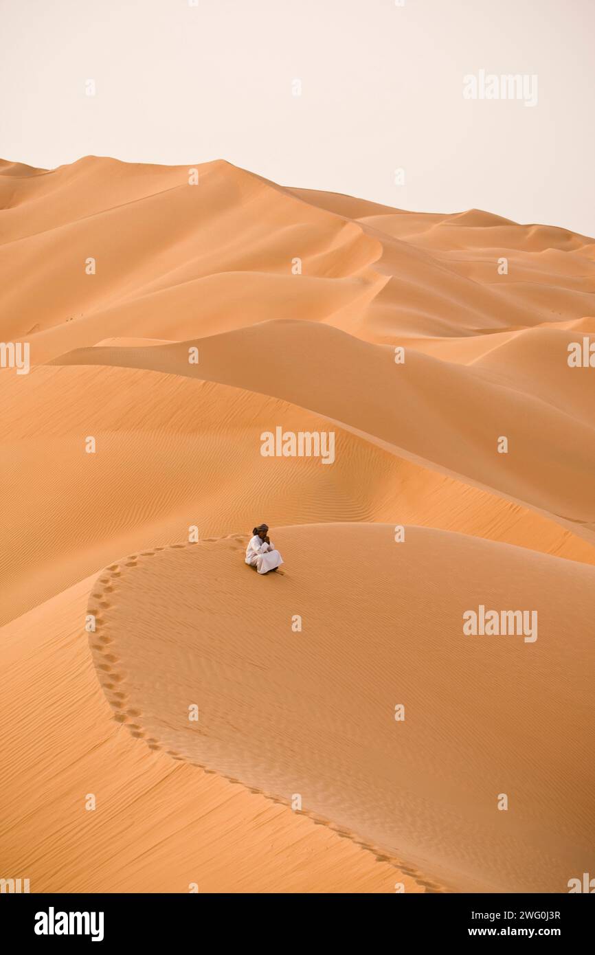 Ein Mann sitzt allein auf den Sanddünen des leeren Viertels, AR Rub Al Khali, Oman. Stockfoto