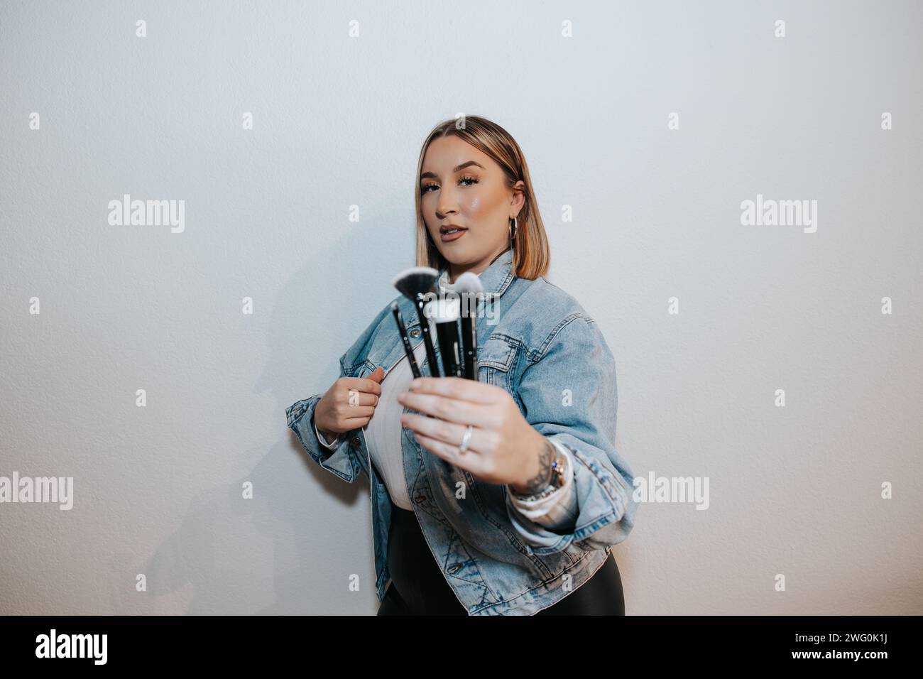 Mädchen mit kurzen blonden Haaren, jeansjacke, Schminkbürsten Stockfoto