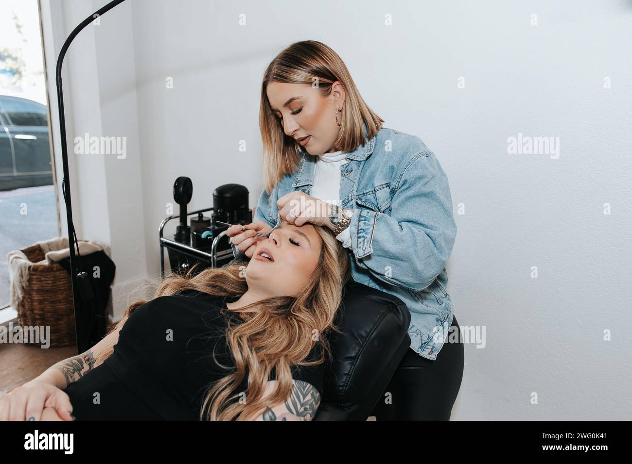 Mädchen mit kurzen blonden Haaren wendet Wimpern auf einen Kunden an, der sich hinlegt Stockfoto