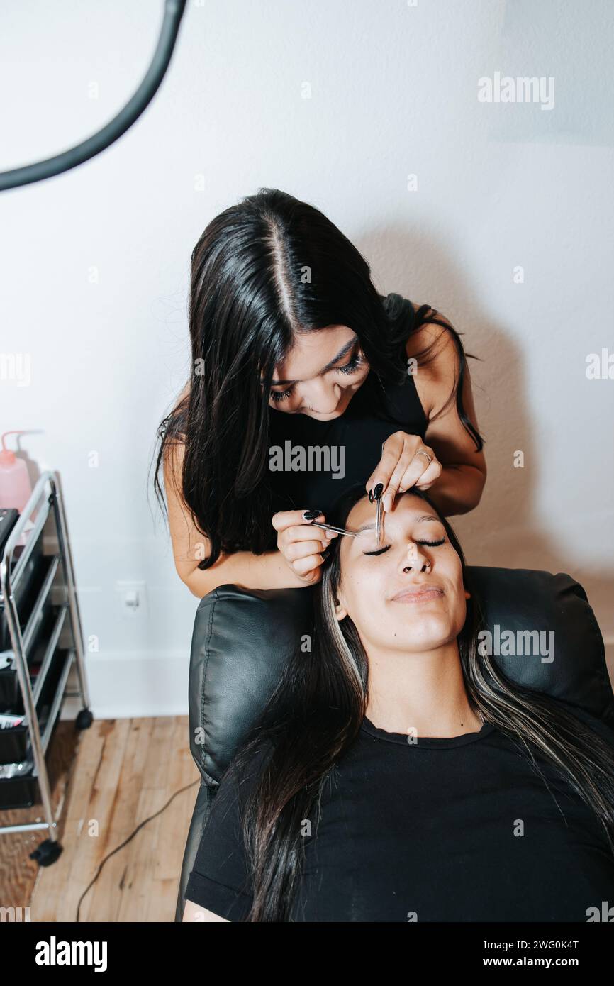 Mädchen mit langen schwarzen Haaren, in stilvoller schwarzer Kleidung, arbeitet an Wimpern Stockfoto
