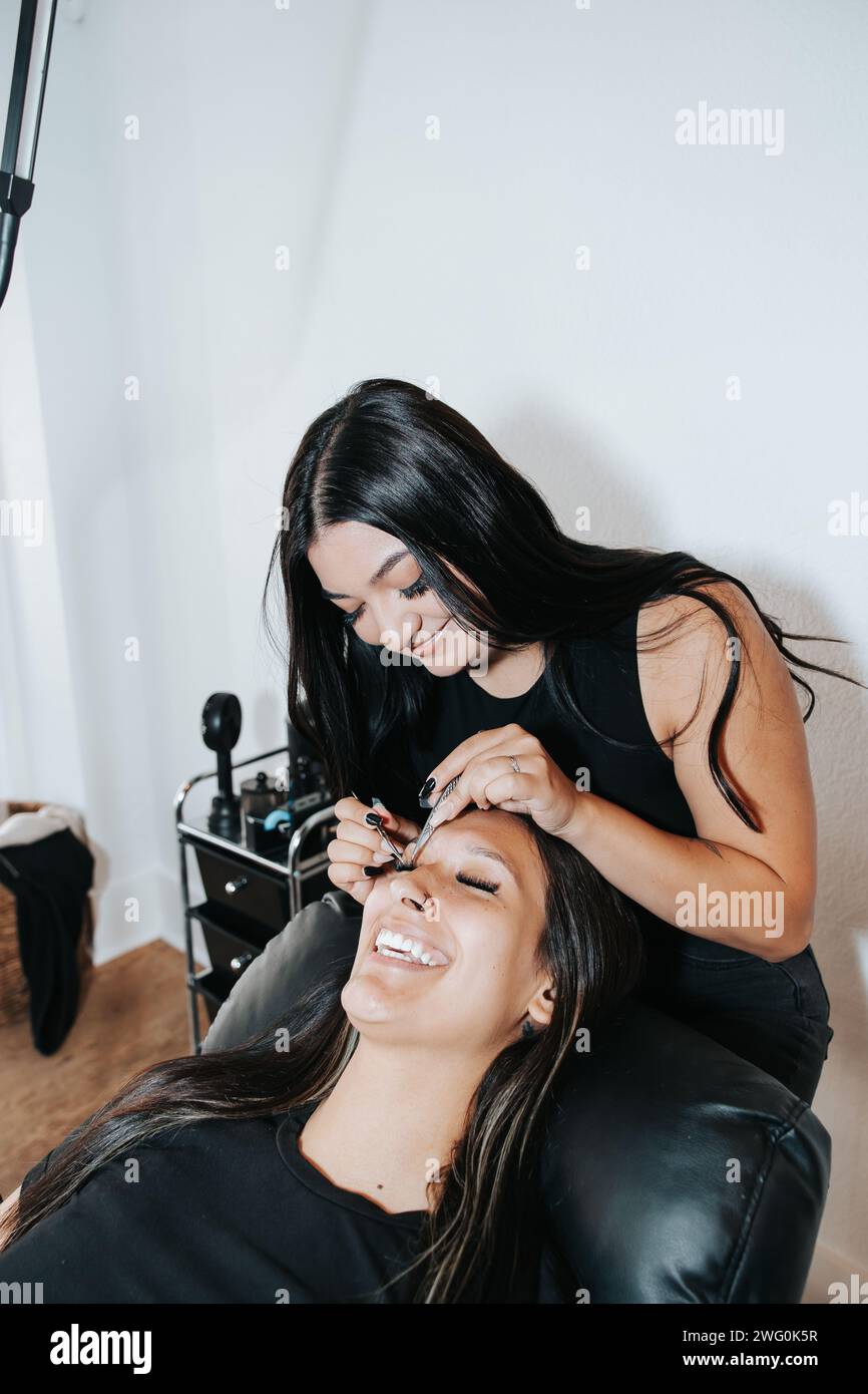 Mädchen mit langen schwarzen Haaren, in stilvoller schwarzer Kleidung, arbeitet an Wimpern Stockfoto