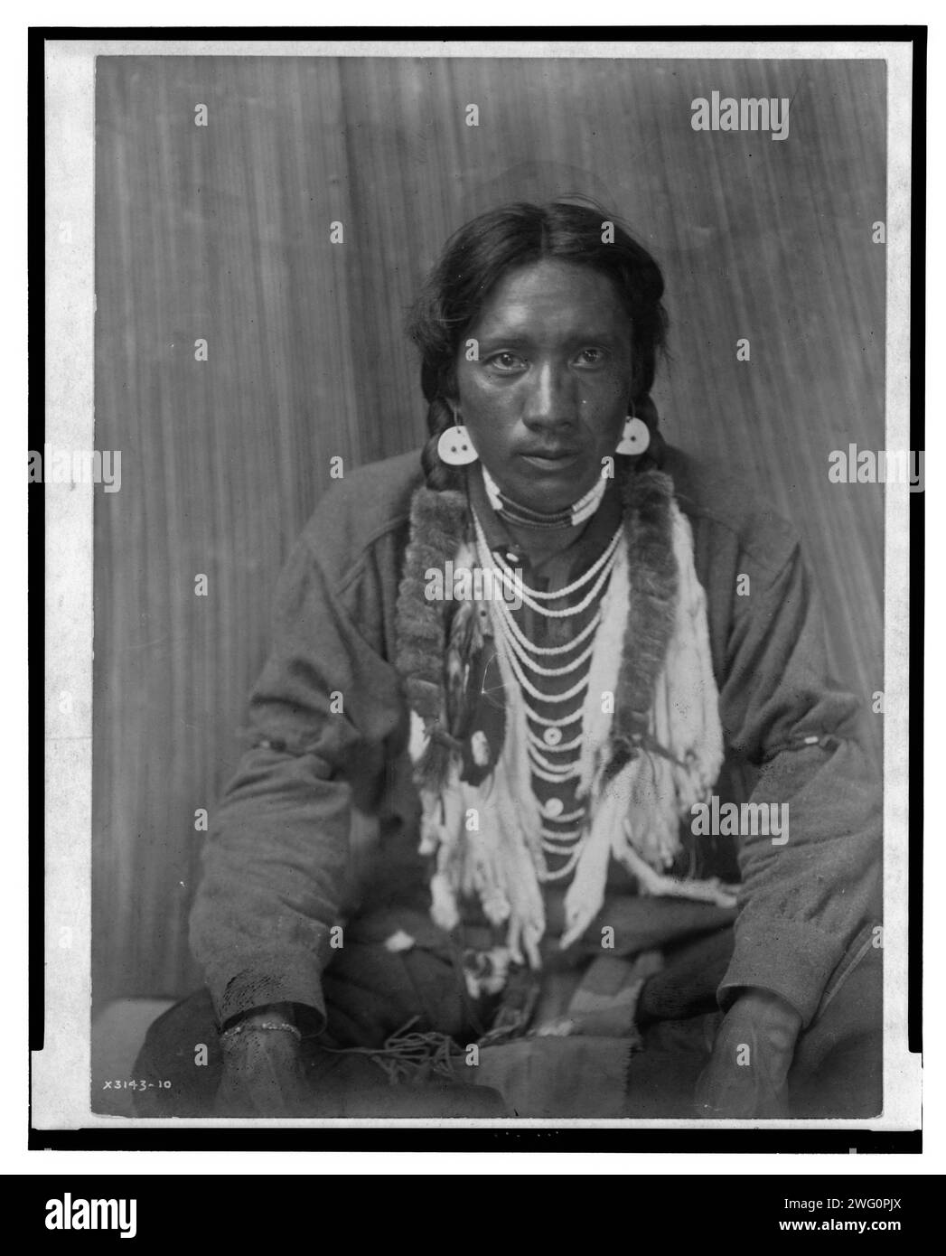 Hemd - Kalispel, 1910. Das Foto zeigt einen Kalispel-Mann, in voller Länge Porträt, nach vorne gerichtet, mit überkreuzten Beinen sitzend, Hände auf Knien. Stockfoto