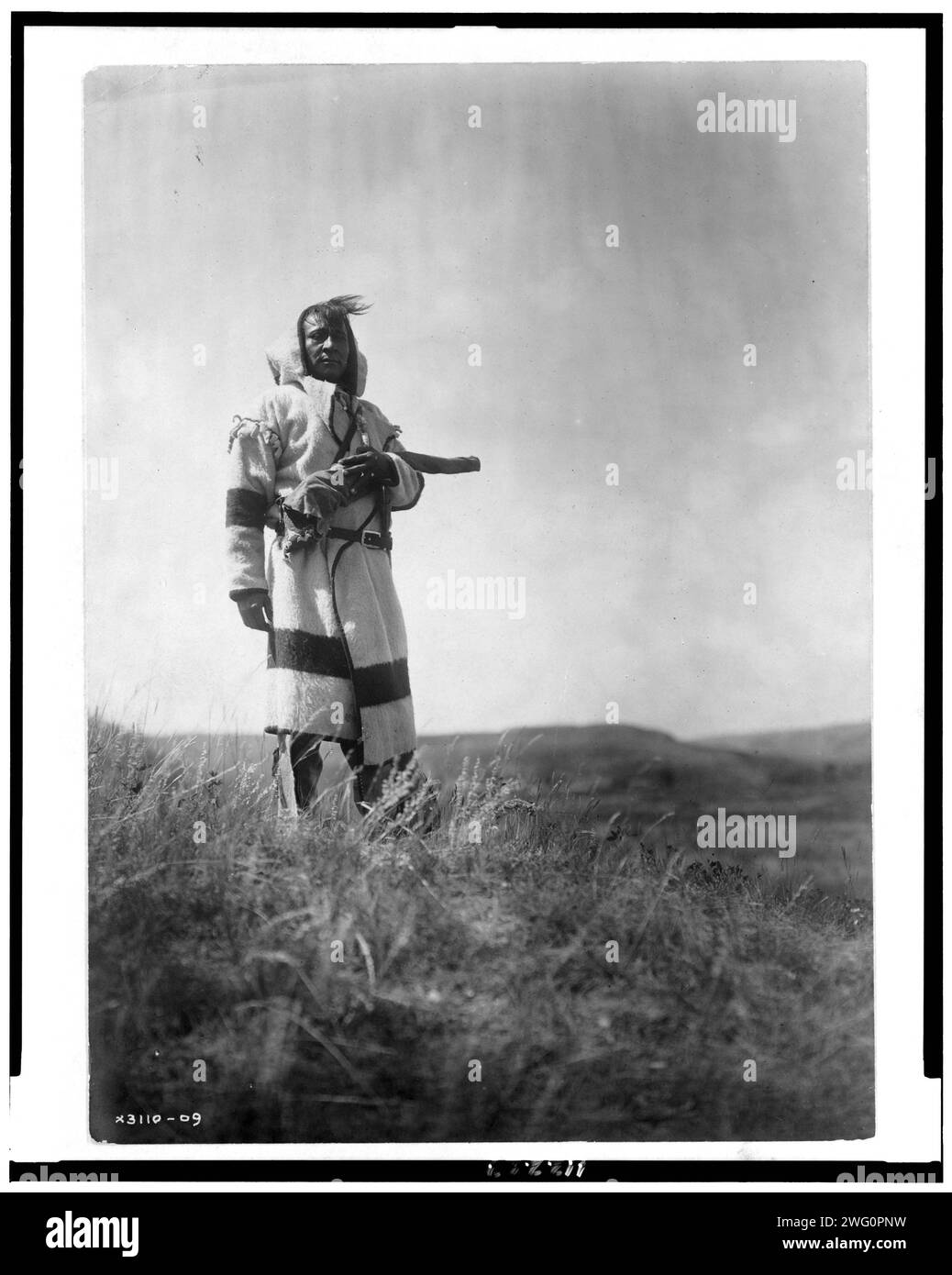 Piegan-Pfadfinder, 1910. Piegan-Mann steht mit offener Prärie hinter ihm. Stockfoto