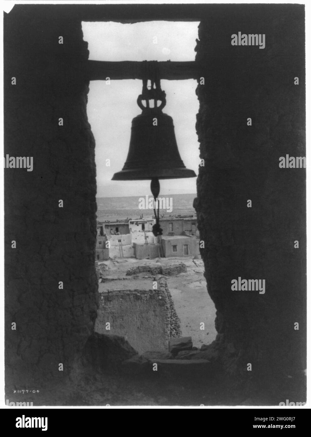 Der alte Glockenturm, 1905. Glocke in der Wand, Pueblo-Gebäude im Hintergrund. Stockfoto