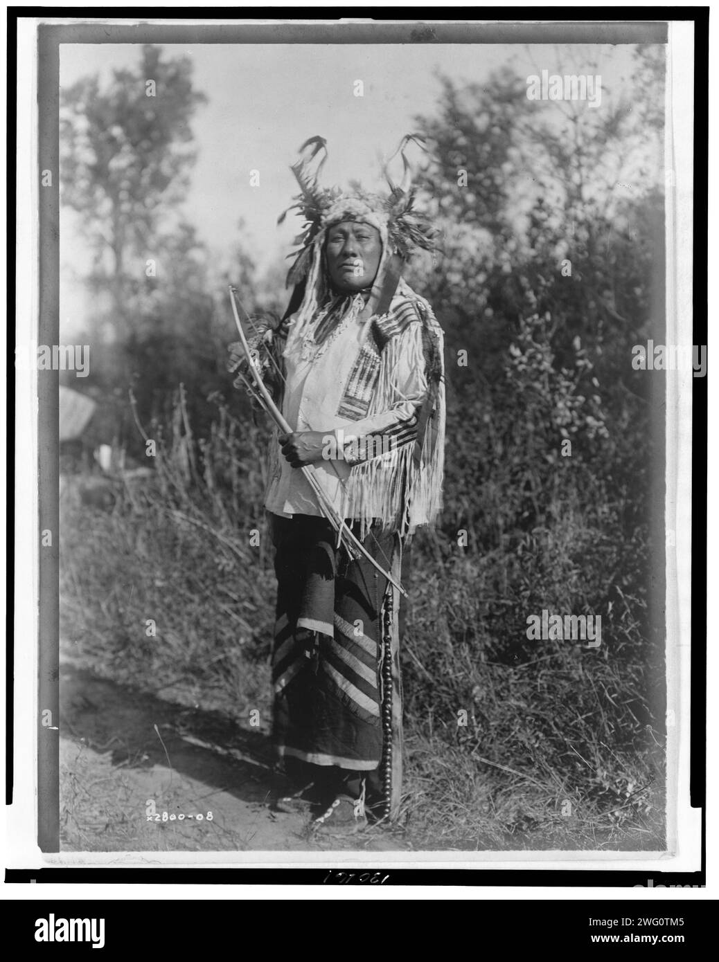 Long Time Dog-Hidatsa, 1908. Langhund, Porträt in voller Länge, stehend, nach vorne gerichtet, Kopfkragen getragen, Hemd aus Buckskin und Leggings mit Messingglocken. Stockfoto