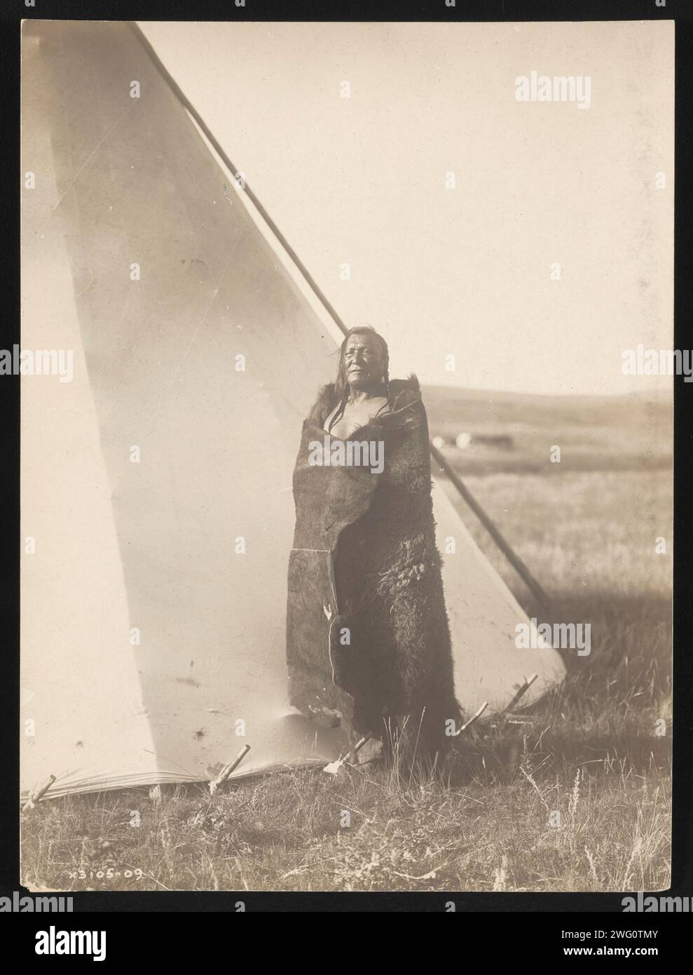 Berghäuptling, 1910. Das Foto zeigt den Berghäuptling, eingewickelt in Büffelfell, der außerhalb des Tipi steht. Stockfoto