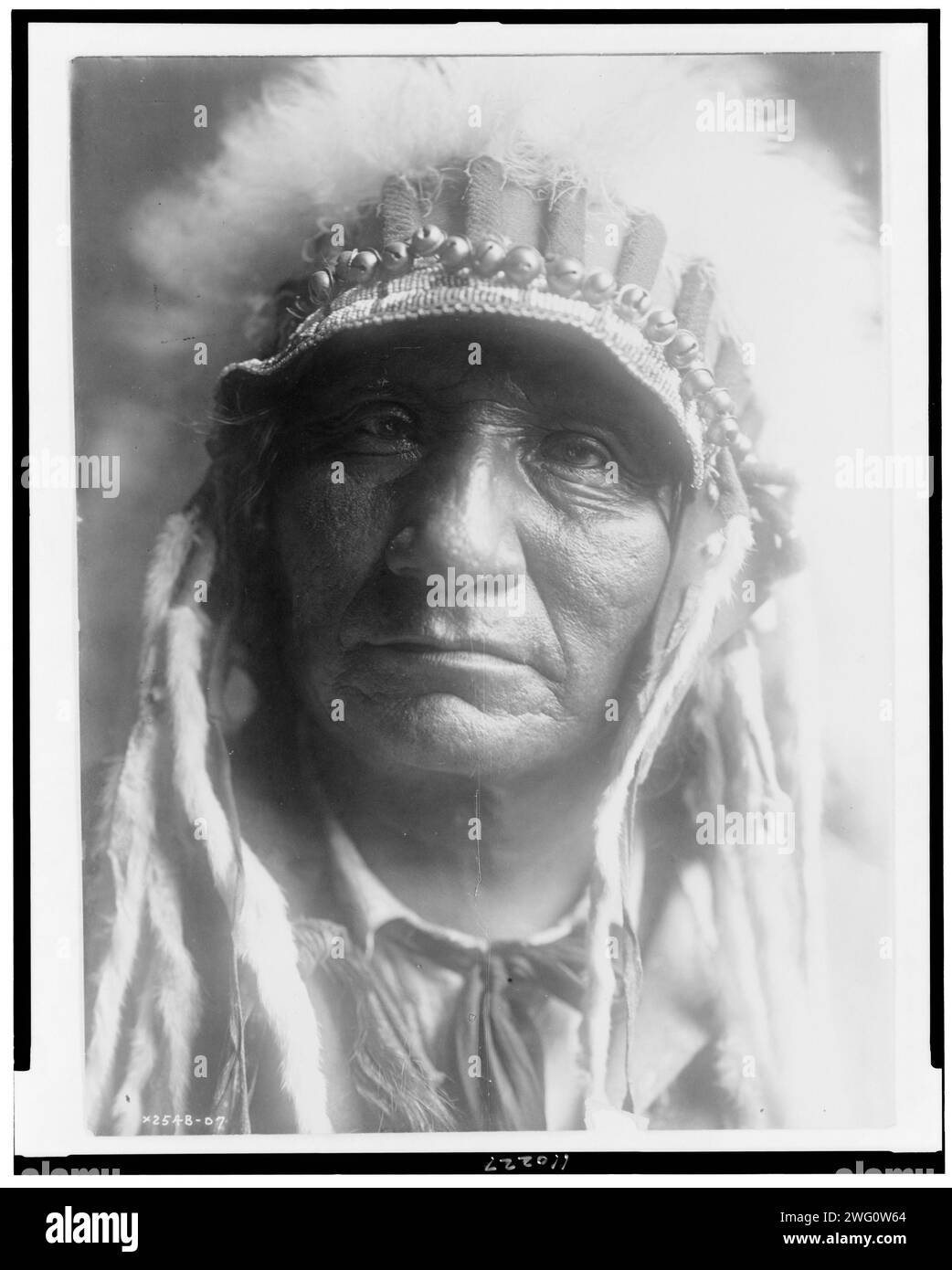 Red Hawk (Che-tan Luta)-Oglala, um 1907. Red Hawk, Oglala Sioux Indianer, Kopf-und-Schultern-Porträt, nach vorne gerichtet, mit Federkopfschmuck. Stockfoto