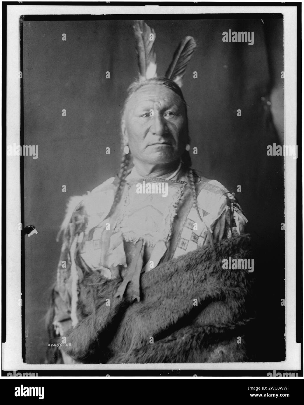 Gelbes Pferd-Yanktonai, halblanges Porträt, stehend, leicht nach rechts gerichtet, mit langen Zöpfen, zwei Adlerfedern im Haar, in Büffelhaut gehüllt, um 1908. Stockfoto