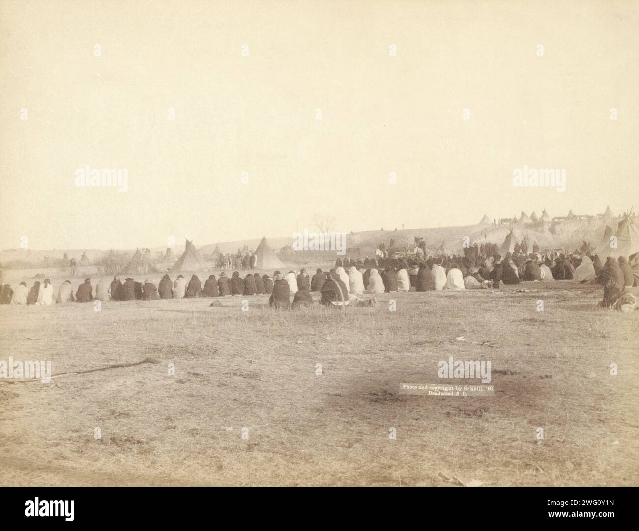 Indianerrat im feindlichen Lager, 1891. Rückansicht eines großen Halbkreises von Lakota-Männern, die auf dem Boden sitzen, mit Tipis im Hintergrund, wahrscheinlich auf oder in der Nähe des Pine Ridge Reservation. Stockfoto