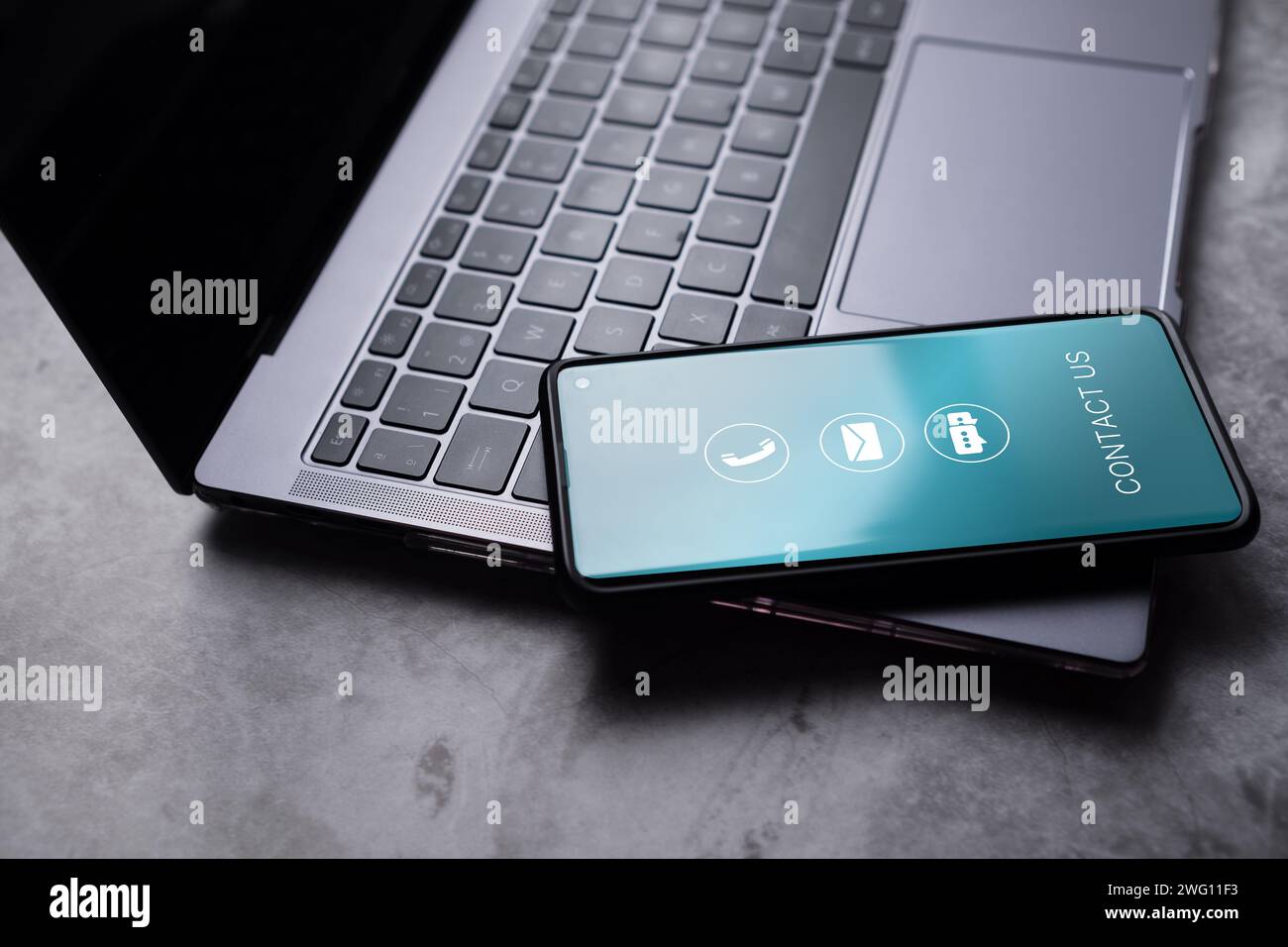 Kontaktieren Sie uns oder das Hotline-Konzept für den Kundendienst. Smartphone auf Laptop mit Kontaktsymbolen auf dem Bildschirm. E-Mail, Adresse, Live-Chat, Anruf. Stockfoto