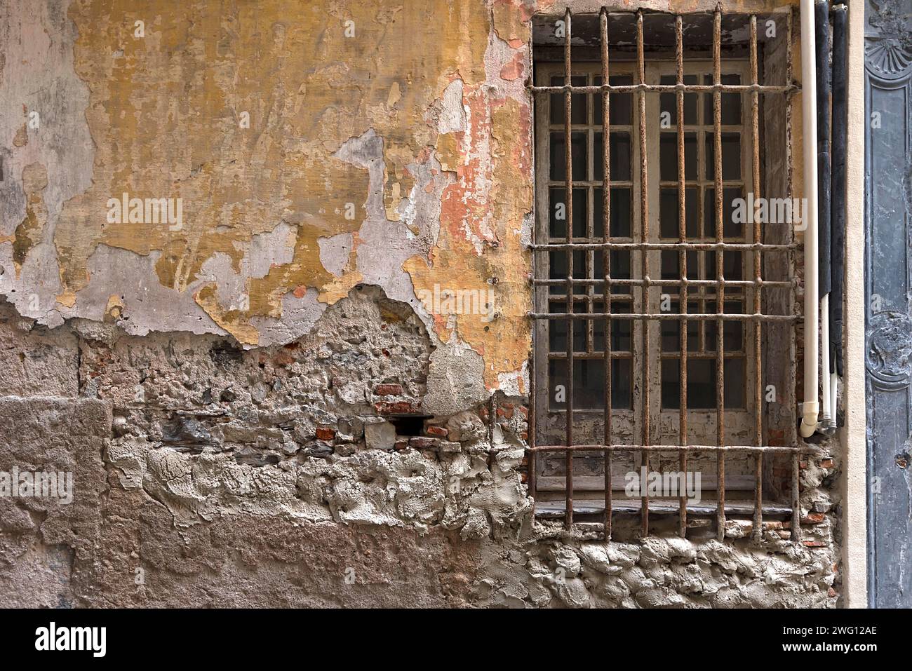 Zerbröckelnde Hausmauer mit einem Gitterfenster in der Altstadt, Genua, Italien Stockfoto