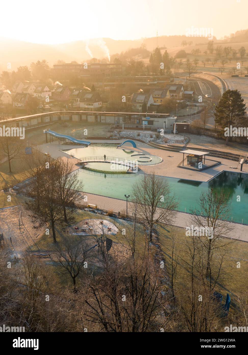 Die niedrige Sonne scheint durch Dunst über einem Schwimmbad in einer kleinen Stadt, ENCW Freibad Calw, Stammheim, Schwarzwald, Deutschland Stockfoto Die niedrige Sonne scheint durch Dunst über einem Schwimmbad in einer kleinen Stadt, ENCW Freibad Calw, Stammheim, Schwarzwald, Deutschland Stockfoto