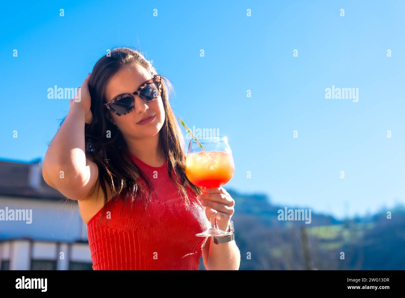 Schicke Frau mit Sonnenbrille, die im Sommer mit einem Cocktail auf einem Dach posiert Stockfoto