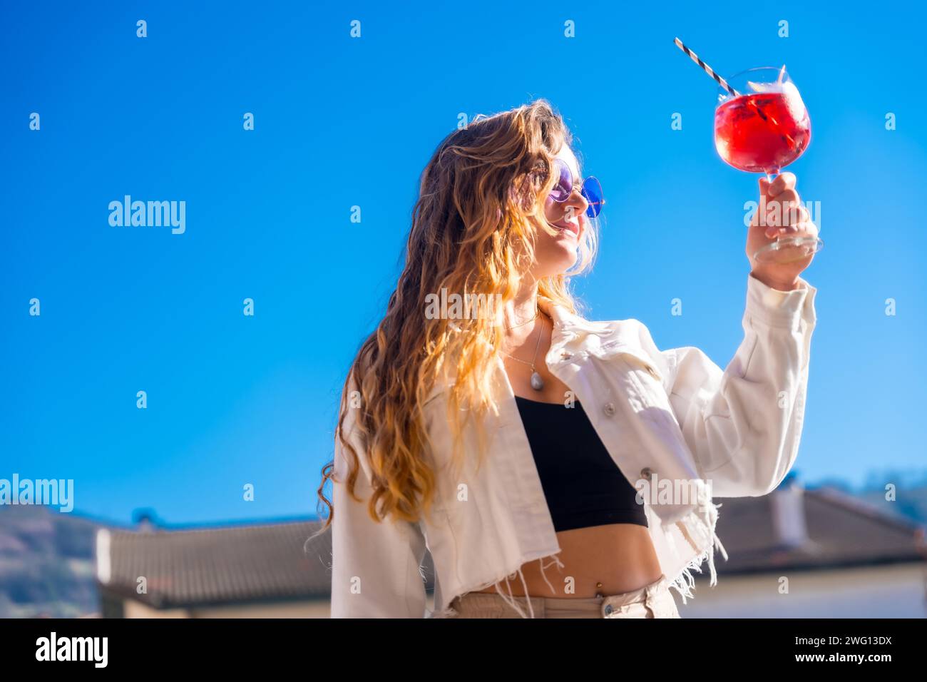 Blonde coole Frau, die während einer Sommerparty auf dem Dach ein Cocktailglas hochhebt Stockfoto