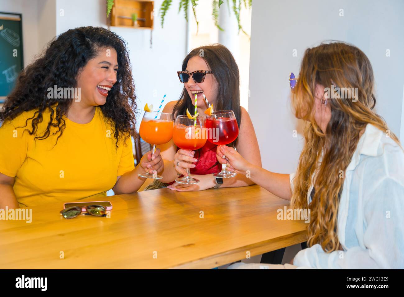 Drei weiße Schönheitsfreunde, die im Sommer in einer Bar mit Cocktails tosten Stockfoto