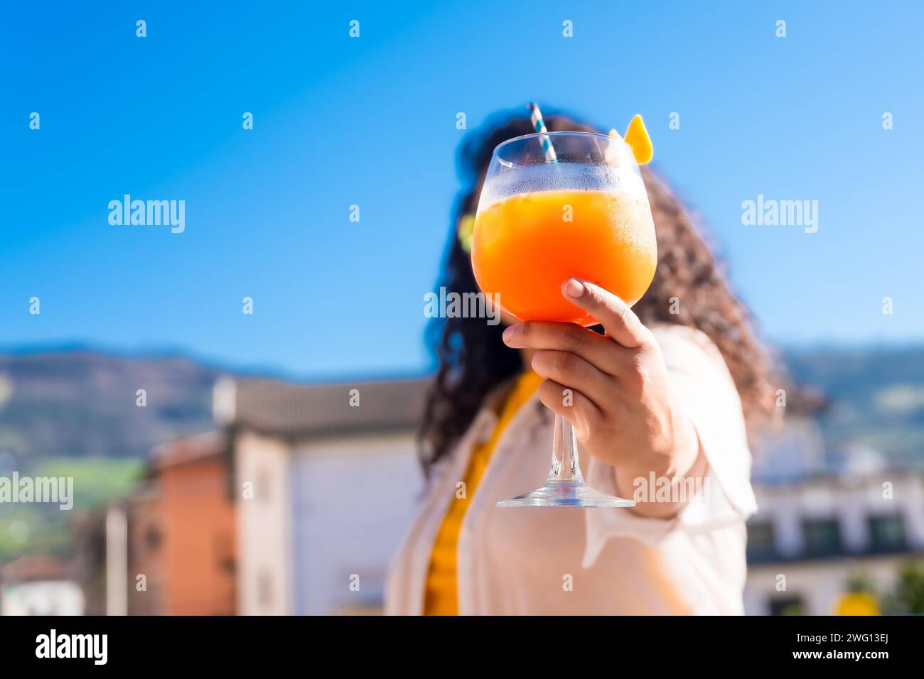 Unerkennbare Frau, die ein Gesicht versteckt und einen Cocktail auf einem Dach hält Stockfoto