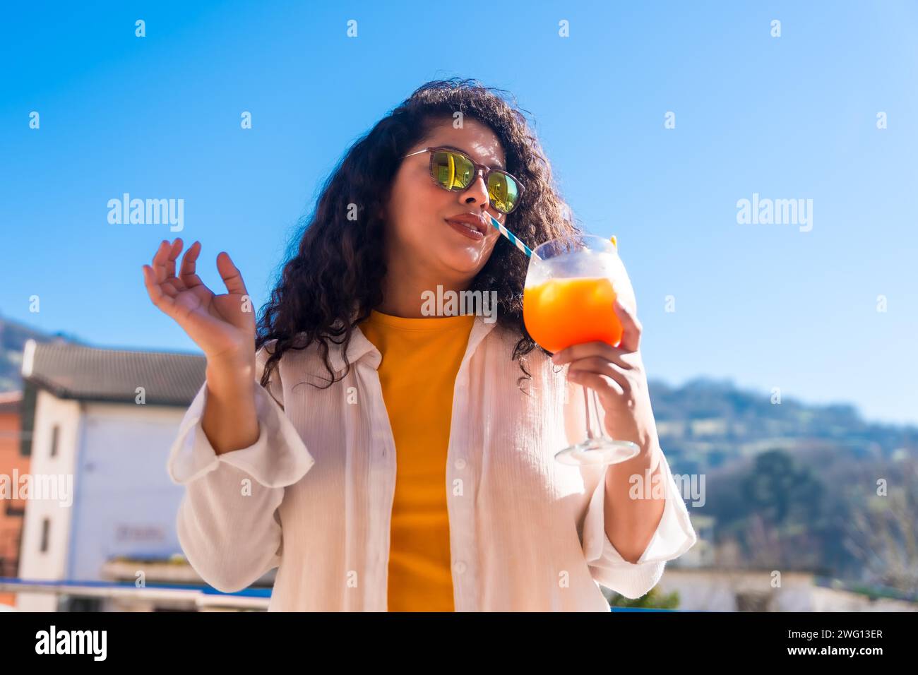 Coole Frau, die einen Cocktail mit Strohhalm auf einem Dach lutscht während einer Sommerparty Stockfoto