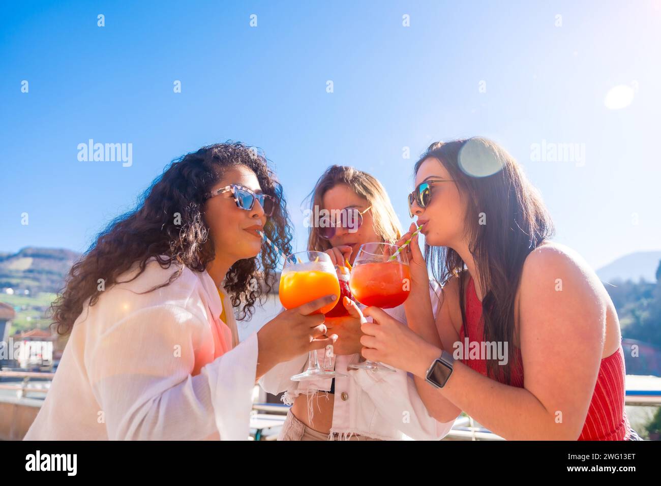 Frauen genießen den Sommer während einer Party und trinken Cocktails zusammen mit Stroh auf der Dachterrasse Stockfoto