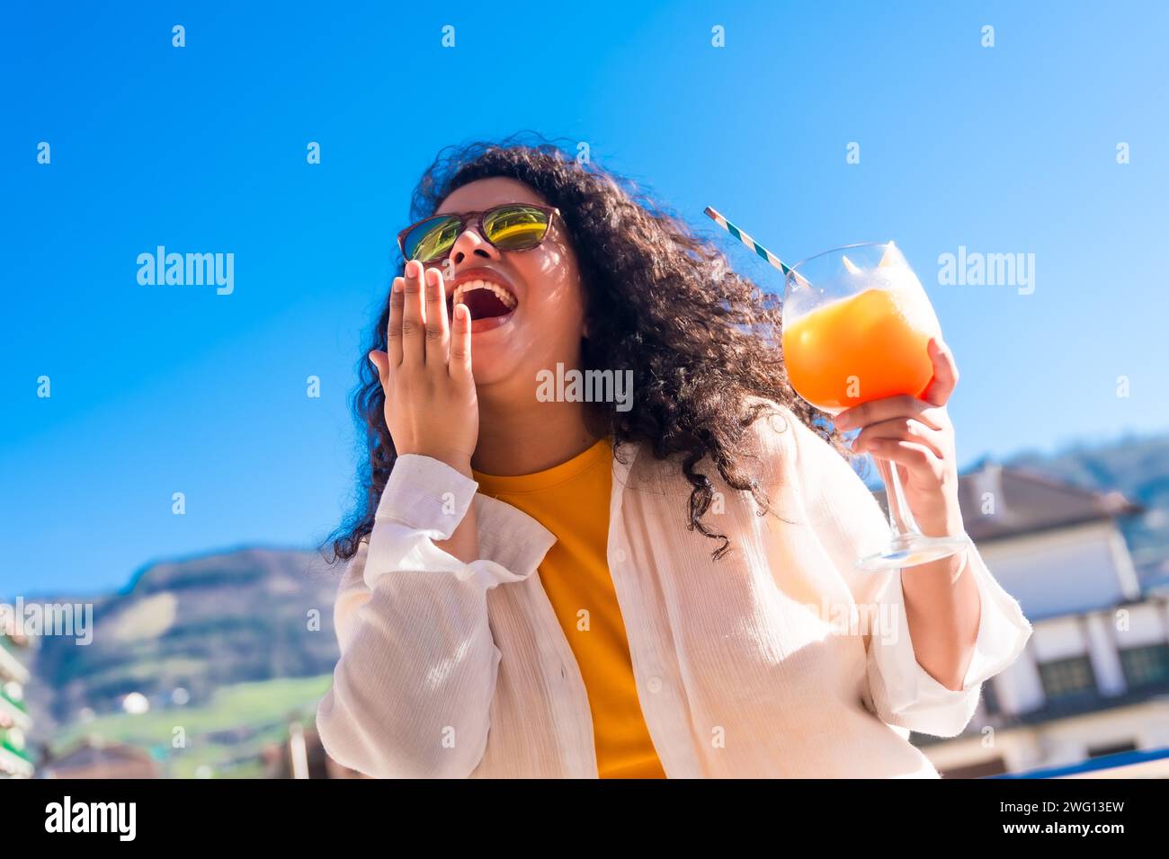 Bewegung und dynamisches Foto einer coolen Frau, die lacht, während sie einen Cocktail auf einem Dach trinkt Stockfoto