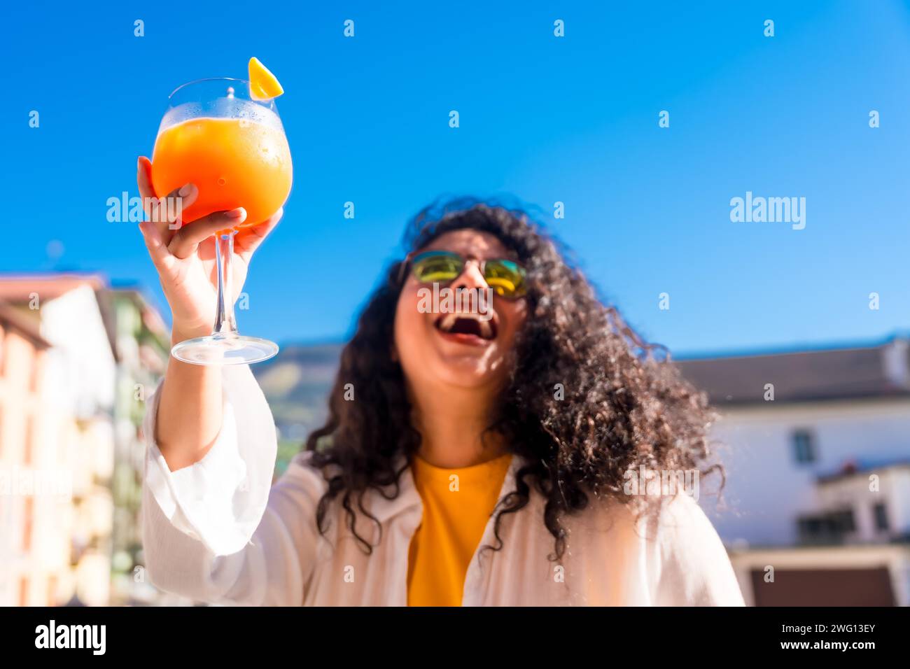Frau mit lässiger Kleidung und Sonnenbrille trinkt Cocktails und genießt eine Sommerparty auf einem Dach Stockfoto