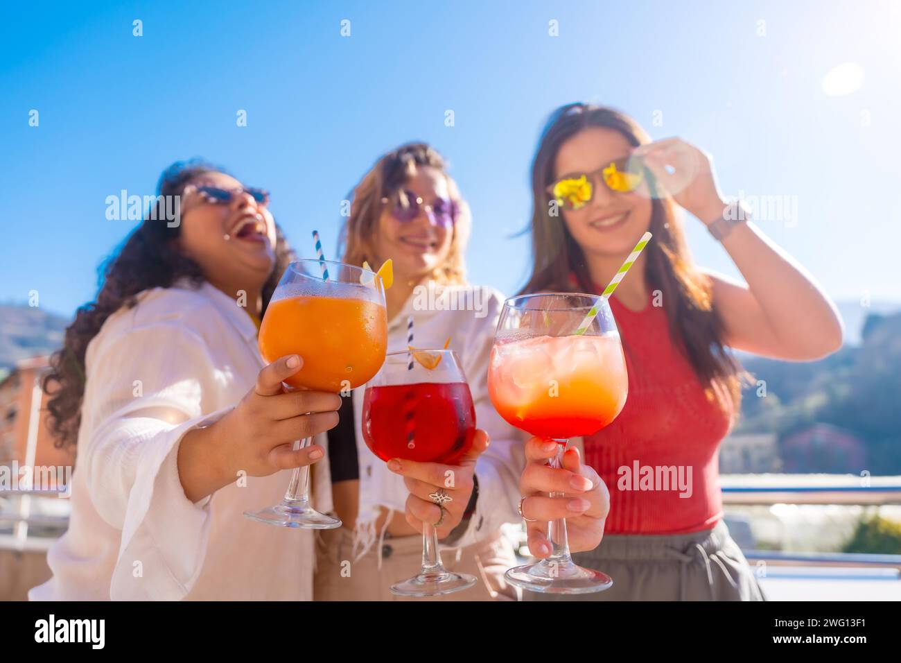 Frontfoto von drei Freundinnen, die Cocktails trinken und im Sommer Spaß auf einem Dach haben Stockfoto