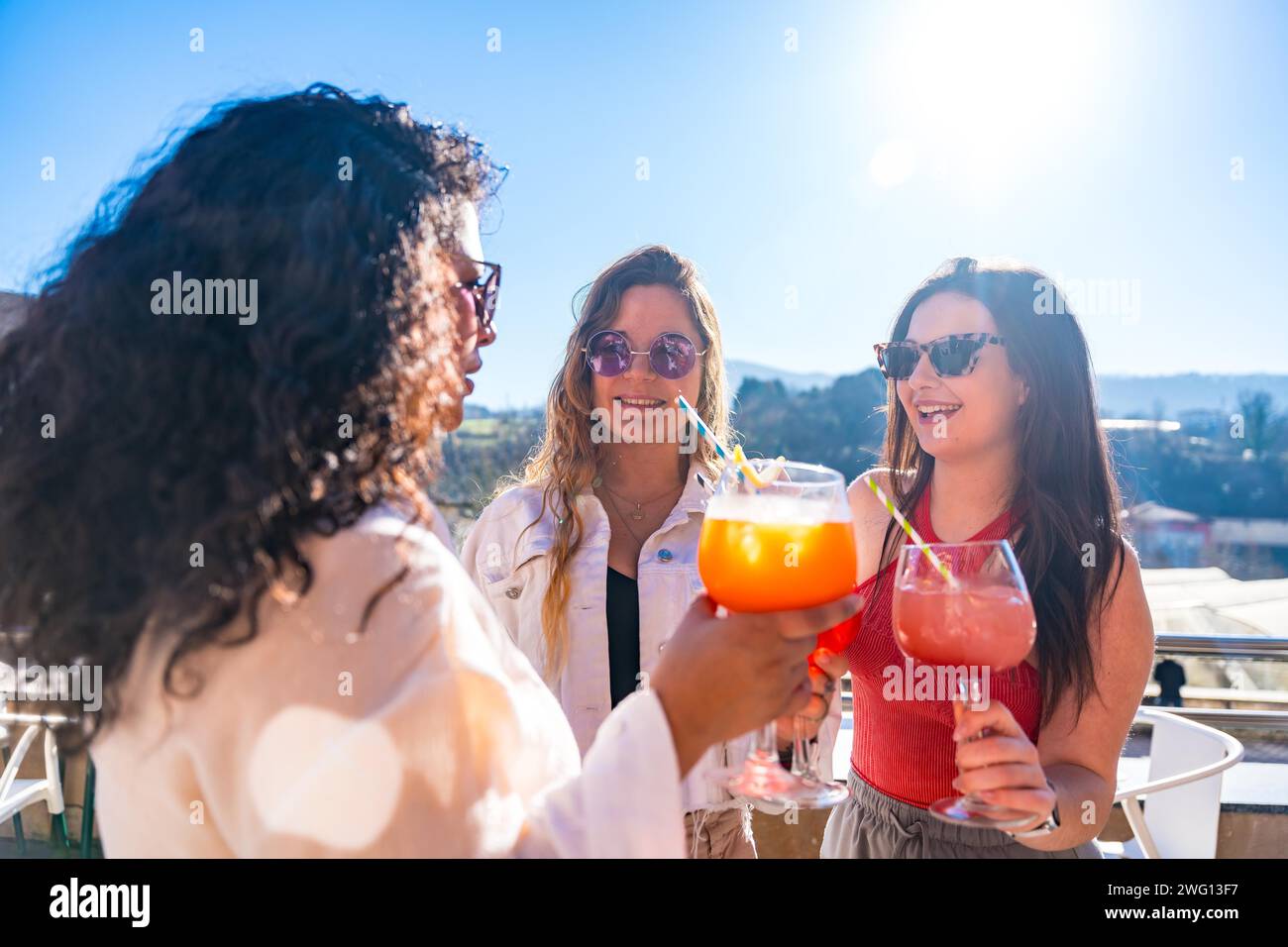 Drei coole Freundinnen genießen an einem sonnigen Tag den Sommer mit Cocktails auf einem Dach Stockfoto