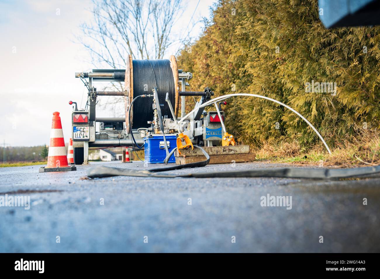 Straßenarbeitsgeräte mit nasser Oberfläche und Kabeltrommel im Vordergrund, Glasfaserbau, Nagold, Schwarzwald, Deutschland Stockfoto