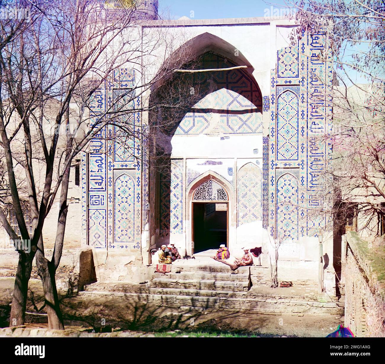 Haupteingang zur Shakh-i Zindeh Moschee, Samarkand, zwischen 1905 und 1915. Männer sitzen auf Treppen unter dem Torbogen in der Shah-i-Zinda Nekropole. Das Shah-i-Zinda Ensemble umfasst Mausoleen und andere rituelle Gebäude aus dem 11. Bis 15. Und 19. Jahrhundert. Stockfoto