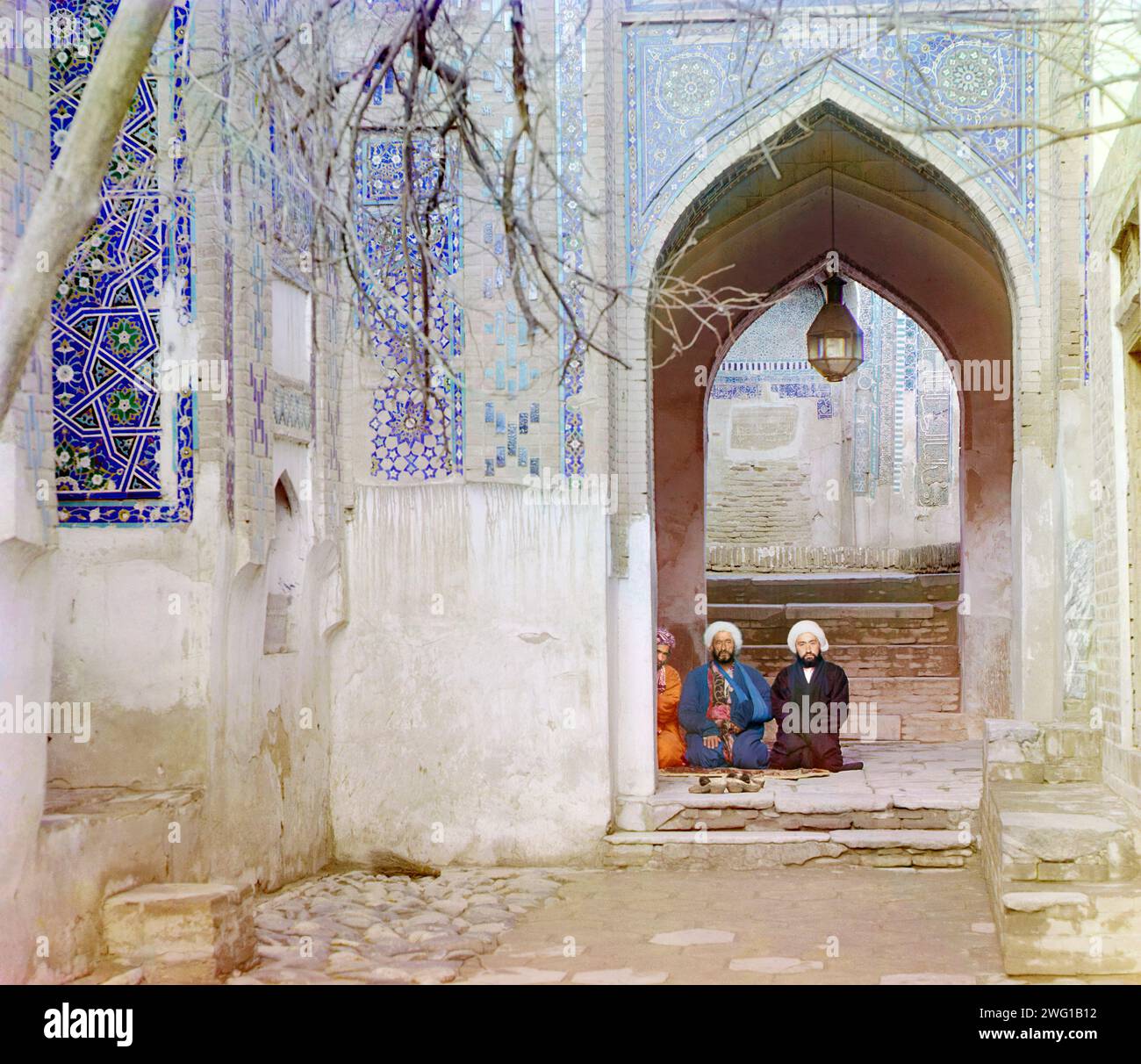 Am Eingang zum oberen Chartak (Baldachin) von Shakh-i Zindeh, Samarkand, zwischen 1905 und 1915. Männer saßen unter einem Bogen im Shakh-i Zindeh (Shah-i-Zinda) Mausoleum Komplex in Samarkand. Einer der Männer hat seinen Arm in einer Schlinge. Stockfoto