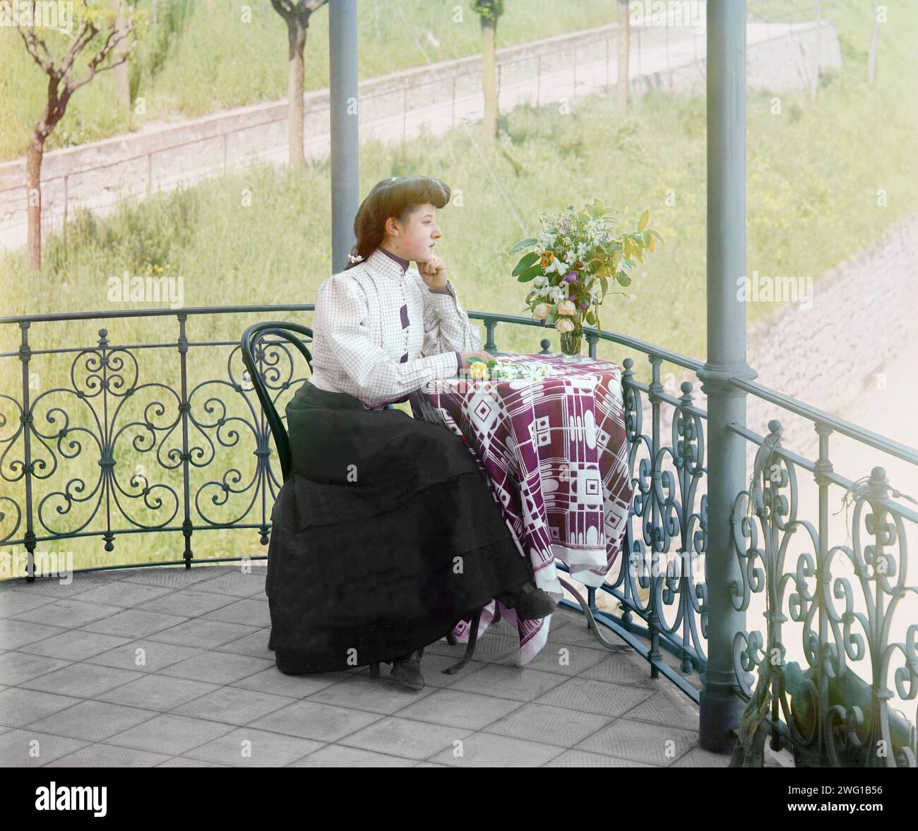 In Italien zwischen 1905 und 1915. Frau in formellem Kleid, posiert, am Tisch mit Blumenvase, auf einem Balkon mit Blick auf ein Feld. Stockfoto